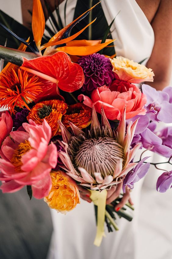 a bold wedding bouquet of a king protea, anthurium, pink peonies, orange, yellow and purple blooms including orchids