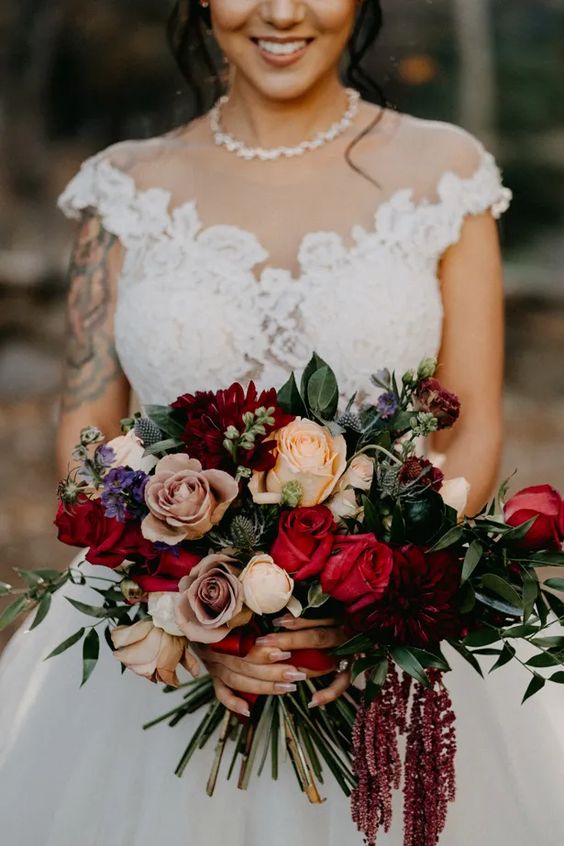 a bold wedding bouquet of peachy, red and coffee-colored roses, purple touches, thistles, greenery and amaranthus