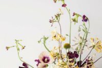 a bold wedding centerpiece of purple sweet peas and yellow and white blooms and greenery is a cool solution for a bold fall wedding