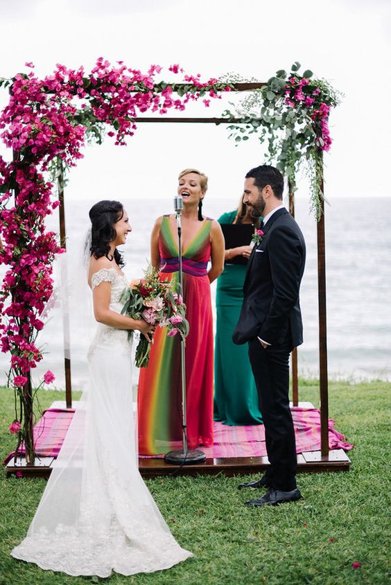 a bold wedding chuppah with bougainvillea and greenery, with a bold rug and a sea view is a cool idea for a bright wedding