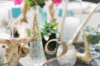 a bright Mediterranean wedding centerpiece of bougainvillea in a tall crystal vase, a candleholder, driftwood and a table number