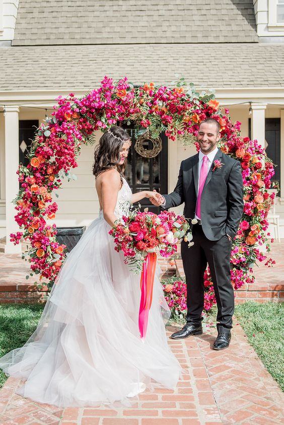 a bright round wedding arch covered with bougainviilea, orange and fuchsia roses and citrus for a colorful summer wedding
