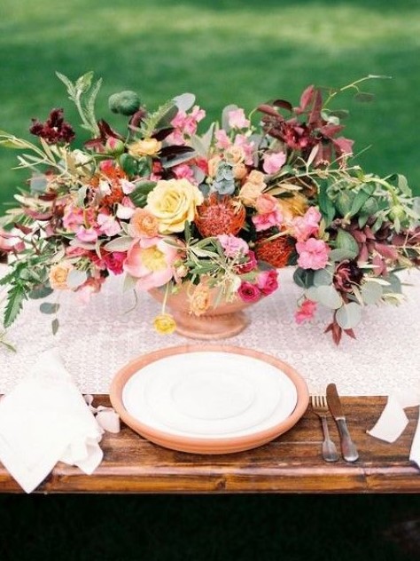 a bright spring wedding centerpiece in yellow, reds, pink, burgundy and with lots of greenery looks warm and cool
