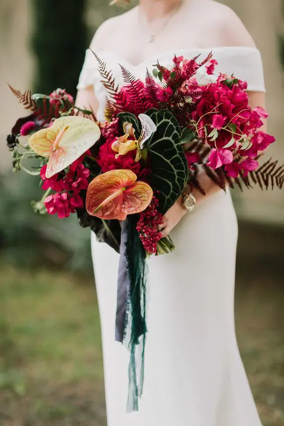 a bright tropical wedding bouquet of yellow anthurium, bold bougainvillea, tropical leaves and fern plus green ribbon