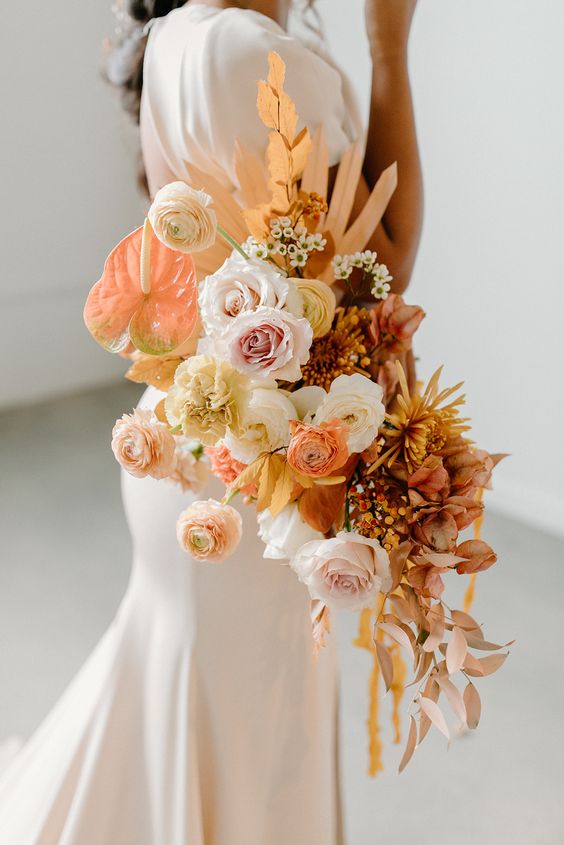 a bright wedding bouquet of blush and peachy blooms, roses and ranunculus, anthurium and dahlias plus fronds