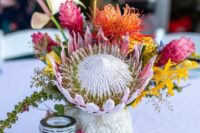 a bright wedding centerpiece of a king protea, bold torpical blooms, anthruiums and greenery is a lovely idea