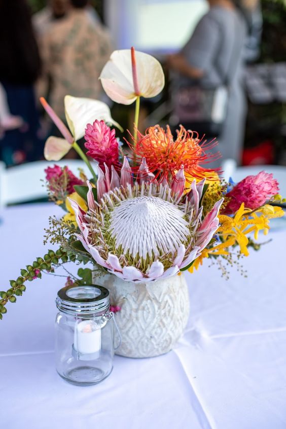 a bright wedding centerpiece of a king protea, bold torpical blooms, anthruiums and greenery is a lovely idea