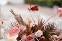 a bright wedding centerpiece of pink carnations, anthurium, dark leaves, dried fronds will be cool for a fall wedding