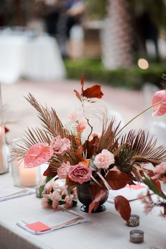 a bright wedding centerpiece of pink carnations, anthurium, dark leaves, dried fronds will be cool for a fall wedding