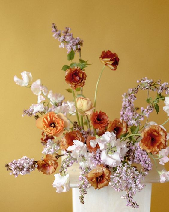 a bright wedding centerpiece of rust and orange tulips, white sweet peas and some lilac fillers is adorable for a spring wedding