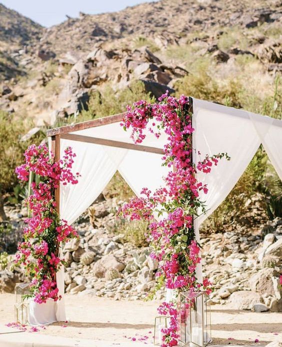 a bright wedding chuppah covered with white fabric and with bougainvillea covering the pillars, with candle lanterns around for a summer wedding