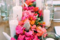 a bright wedding table runner of greenery, bougainvillea and orange blooms plus candles along it for a tropical wedding