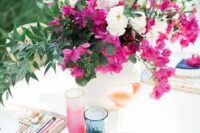 a bright wedding tablescape with a bold magenta centerpiece and matching glasses, colorful placemats and blue napkins