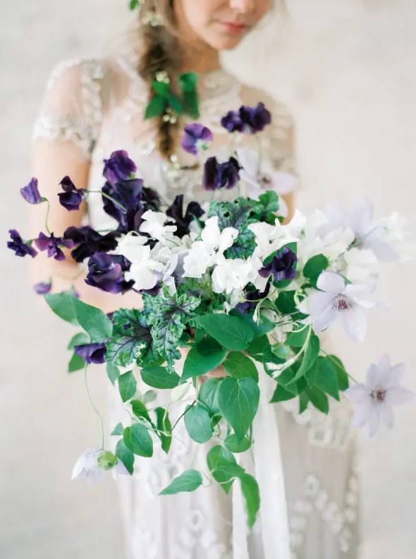 a catchy and contrasting wedding bouquet with deep purple and white blooms and various types of greenery cascading is amazing