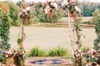 a catchy boho wedding arch of white, peachy, pink and burgundy blooms, greenery, twigs and amaranthus and a boho rug
