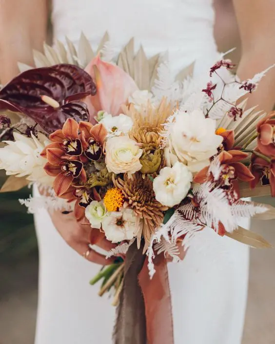 a catchy fall wedding bouquet of white and rust blooms, burgundy anthurium and liles, dried fronds and leaves