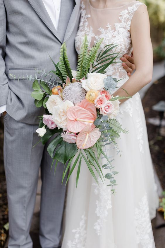 a catchy wedding bouquet of blush anthurium, white and pink roses, yellow ranunculus, greenery and leaves
