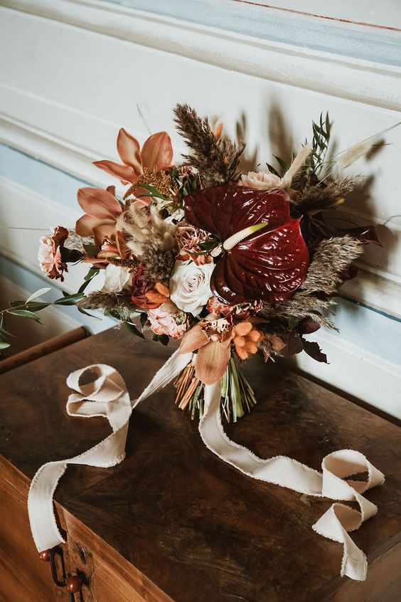 a catchy wedding bouquet of burgundy anthurium, rust lilies and dried and fresh blooms and grasses plus ribbons