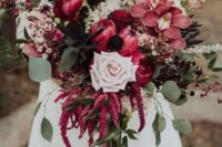 a catchy wedding bouquet of king proteas, orchids, a pale blush rose, dried bloom branches, amaranthus and greenery for the fall