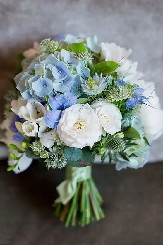 a catchy wedding bouquet of white blooms, blue hydrangeas, greenery and thistles is a stylish and chic idea with plenty of texture