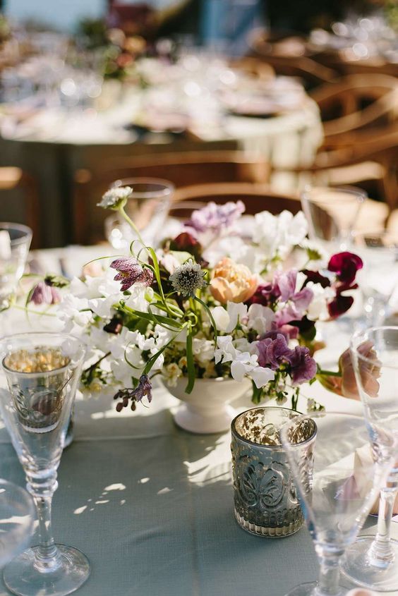 a catchy wedding centerpiece of allium, white and purple sweet peas, greenery and some other blooms mixed for a relaxed look