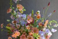 a catchy wedding centerpiece of lilac sweet peas, rust and pink blooms and greenery for a spring or summer wedding