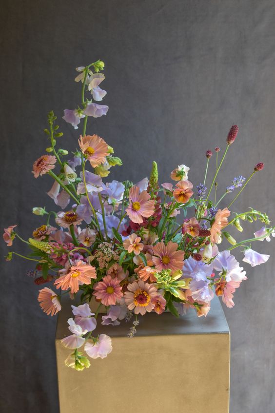 a catchy wedding centerpiece of lilac sweet peas, rust and pink blooms and greenery for a spring or summer wedding