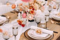 a catchy wedding centerpiece of pink and yellow ranunculus, pink anthuriums, deep purple flowers and some dried elements