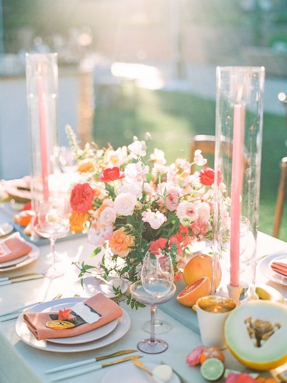 a cheerful summer wedding centerpiece of light pink, red, orange blooms and greenery and pink candles