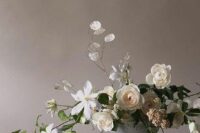 a chic and elegant wedding centerpiece of white roses and other blooms, greenery, berries and lunaria is adorable