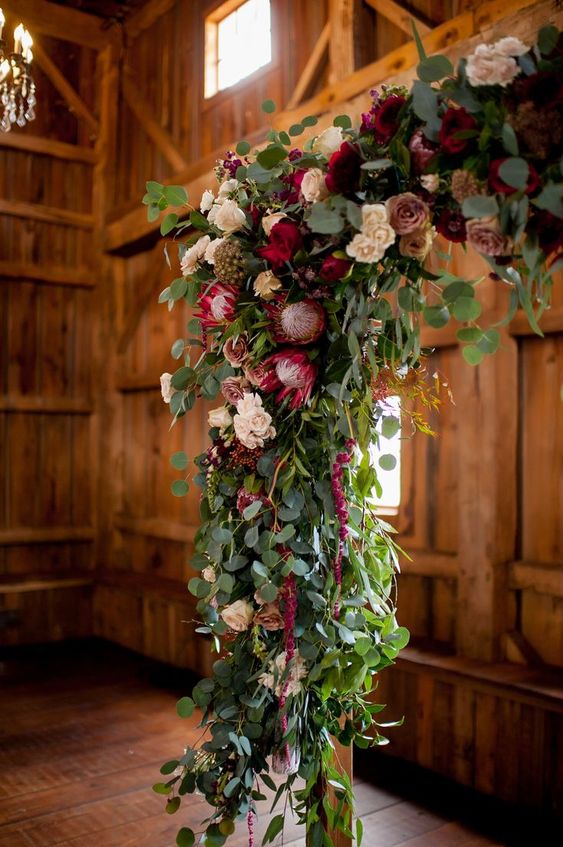 a chic rustic wedding arch with greenery, blush, mauve and burgundy roses, king proteas and amaranthus for a touch of color and texture