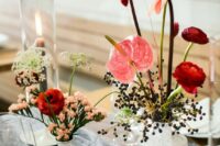 a cluster wedding centerpiece of red ranunculus, berries, anthuriums, twigs and a candle is a whimsical and catchy idea