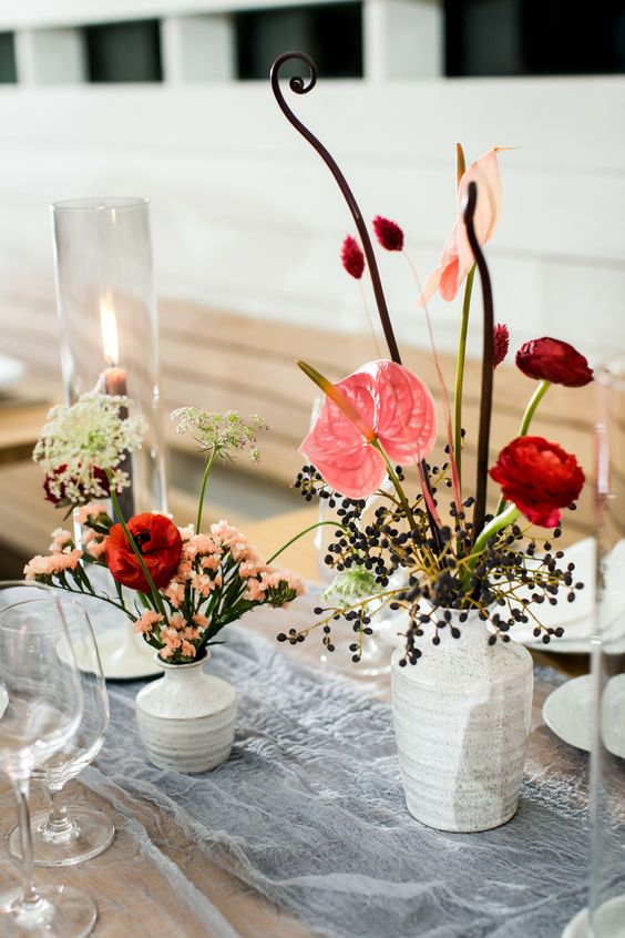 a cluster wedding centerpiece of red ranunculus, berries, anthuriums, twigs and a candle is a whimsical and catchy idea