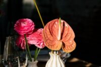 a cluster wedding centerpiece of rust anthuriums and pink ranunculus plus fruits on the table for a tropical wedding