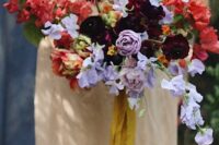 a colorful and contrasting wedding bouquet of red, deep purple, lilac blooms including ranunculus and swete peas is wow