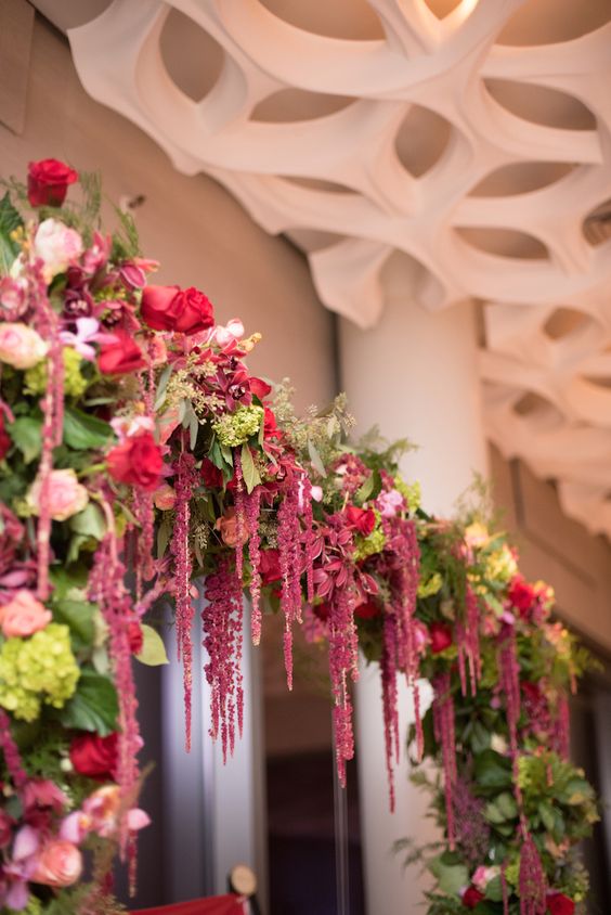 a colorful wedding arch of greenery, red roses and pink ones, amaranthus and some textured foliage is a bold and cool idea for the fall