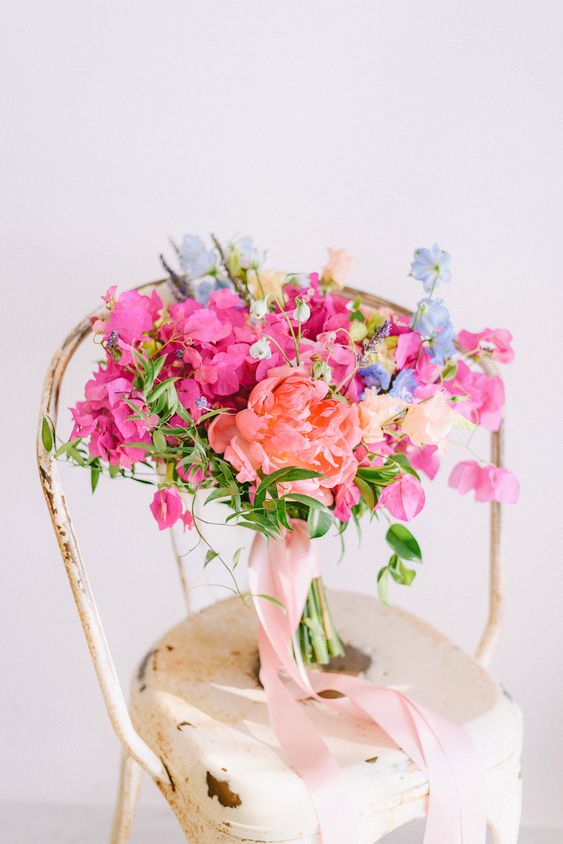 a colorful wedding bouquet of a coral peony, bougainvillea, blue blooms and lavender, greenery is a summer wedding solution