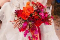 a colorful wedding bouquet of bougainvillea, orange and red roses, baby’s breath, bold orange fronds and bold ribbon