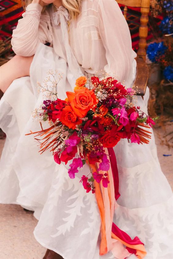 a colorful wedding bouquet of bougainvillea, orange and red roses, baby's breath, bold orange fronds and bold ribbon