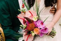 a colorful wedding bouquet of pink orchids, pink anthurium, some greenery and berries and a pincushion protea is wow