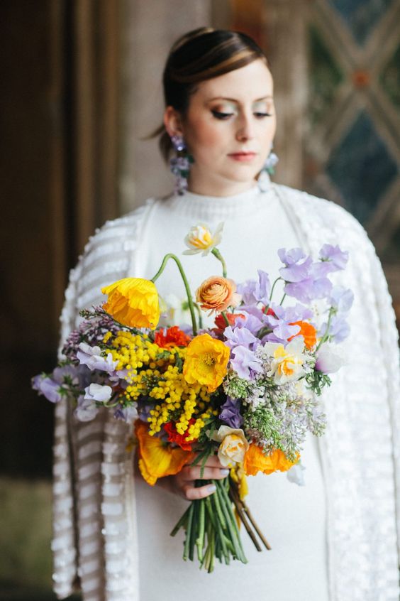 a colorful wedding bouquet of yellow tulips, rust ranunculus, lilac sweet peas, greenery and mimosa for a bright wedding