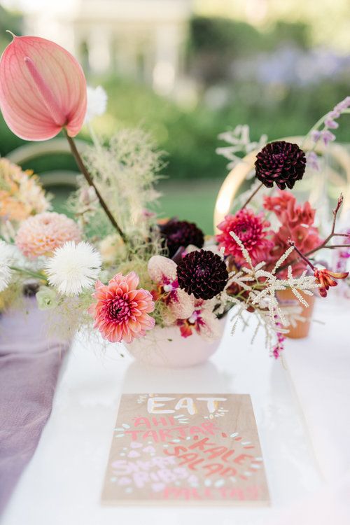 a contrasting wedding centerpiece of pink, deep purple dahlias and mums, greenery, branches and pink anthuriums is wow