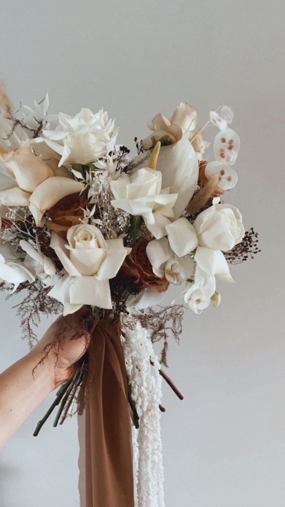 a cool boho wedding bouquet of white roses, anthurium, lunaria, berries and dark coffee-colored roses and matching ribbons