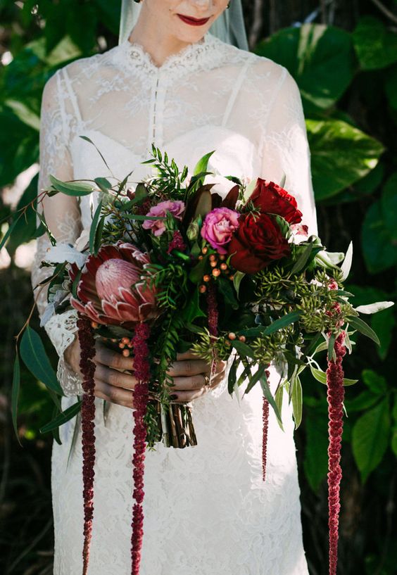 a dark wedding bouquet of king proteas, burgundy and pink roses, greenery and berries and amaranthus for a fall or winter wedding