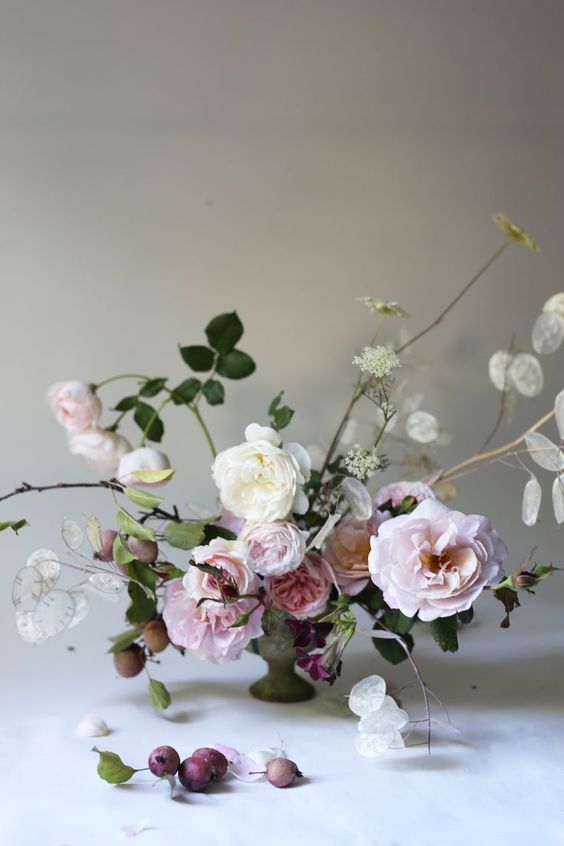 a delicate and subtle wedding centerpiece of blush peony roses and white ones, some greenery and fruit and lunaria is a lovely idea