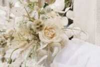 a delicate neutral wedding bouquet of white roses, lunaria, mums, dried white leaves is a cool idea for a spring or summer wedding