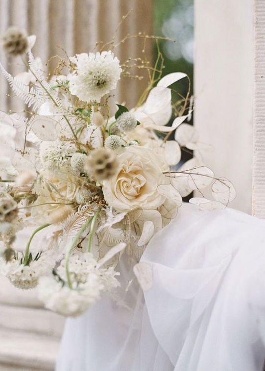 a delicate neutral wedding bouquet of white roses, lunaria, mums, dried white leaves is a cool idea for a spring or summer wedding