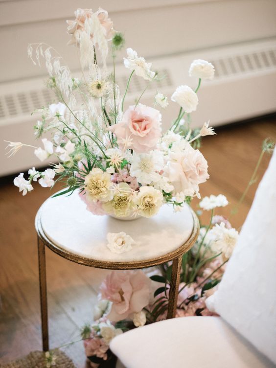 a delicate neutral wedding centerpiece of white ranunculus, white carnations, blush roses, white sweet peas and greenery for spring or summer