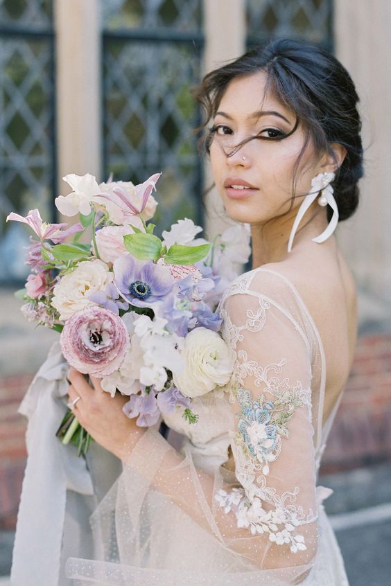 a delicate pastel wedding bouquet of white ranunculus and sweet peas, purple anemones and mauve blooms and greenery for a spring bride