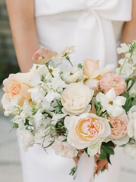 a delicate peach wedding bouquet of white and blush roses and peony roses, carnations and sweet peas blooms